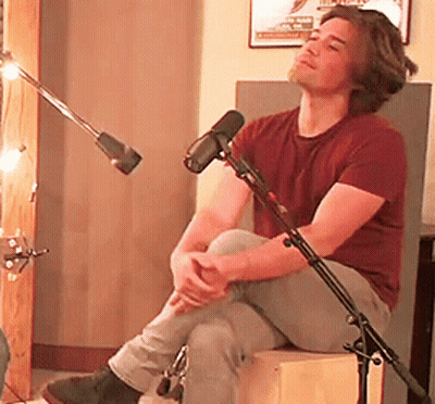 Man In Maroon Shirt Sitting On Box By Microphone GIF