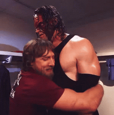 Man In Mask Hugging Man In Maroon Shirt GIF