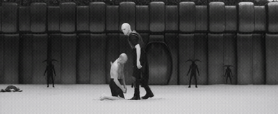 Man In Mask Kneeling Next To Another Man In Black And White Photo GIF