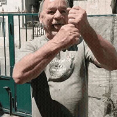 Man In Milano Shirt Standing In Front Of Green Fence GIF