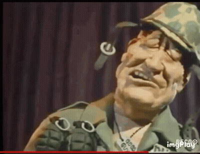 Man In Military Uniform Holding Grenade And Smiling GIF