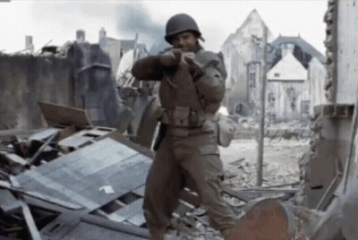 Man In Military Uniform Standing In Destroyed City Holding Gun GIF