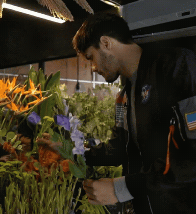 Man In NASA Jacket Looking At Purple Flowers GIF
