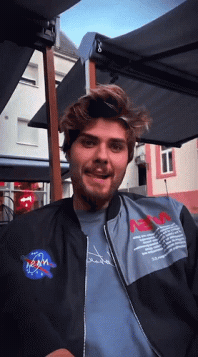 Man In NASA Jacket Sitting Under Umbrella GIF