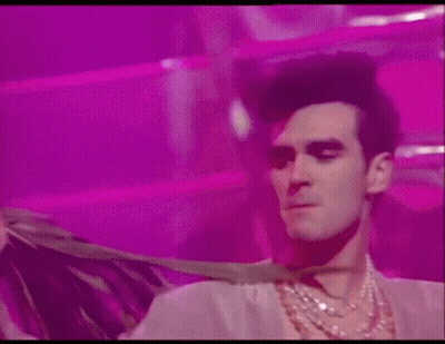 Man In Necklace And Wig Dancing On Pink Background GIF