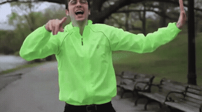 Man In Neon Green Jacket With Arms Outstretched In Park GIF