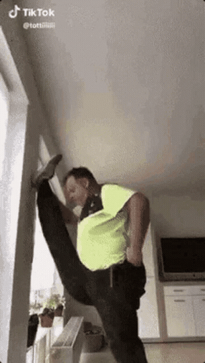 Man In Neon Green Shirt Doing Split In Living Room GIF