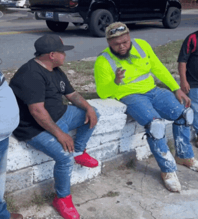 Man In Neon Yellow Shirt Sitting On Wall With Legs Crossed GIF