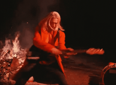 Man In Orange Coat Playing Guitar By Fire GIF