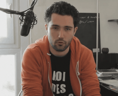 Man In Orange Hoodie And 101 Des Shirt At Microphone GIF