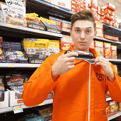 Man In Orange Jacket Holding Candy Bar GIF