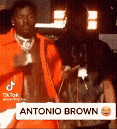 Man In Orange Jacket Next To Man In Dark Room GIF