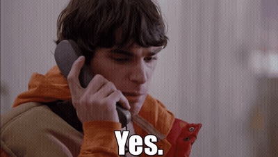 Man In Orange Jacket Talking On Phone Saying Yes GIF