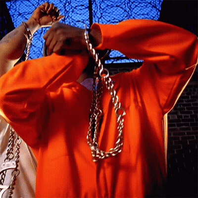 Man In Orange Jumpsuit Chained To Fence GIF