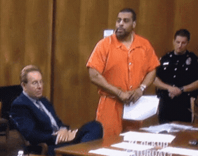 Man In Orange Jumpsuit Standing Before Man In Suit At Table GIF