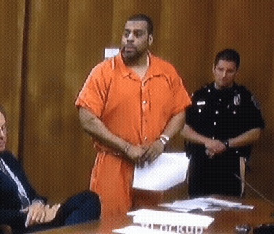 Man In Orange Jumpsuit Standing By Clock Up Sign GIF