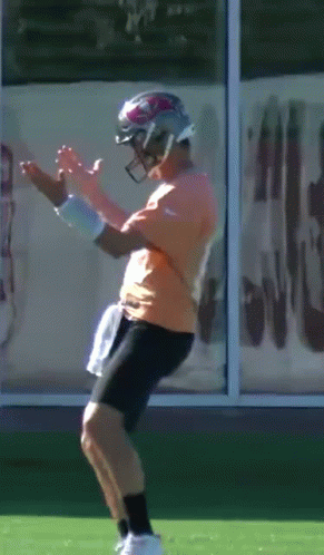 Man In Orange Shirt And Black Shorts Wearing Football Helmet GIF
