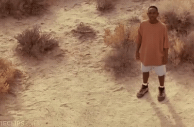 Man In Orange Shirt And White Shorts Standing In Dirt Field GIF
