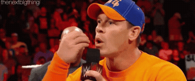Man In Orange Shirt Blue Hat On Mic GIF