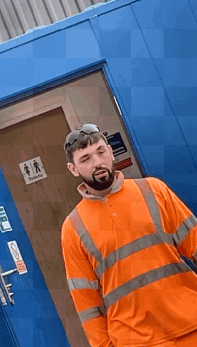 Man In Orange Shirt By Blue Door Saying Toilets GIF