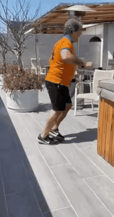 Man In Orange Shirt Doing Squats On Patio GIF