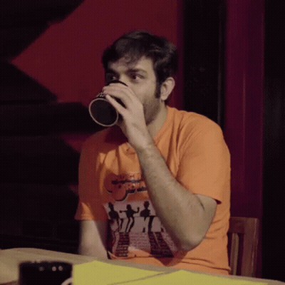 Man In Orange Shirt Drinking From Cup With People Picture GIF