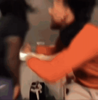 Man In Orange Shirt Holding Arm GIF