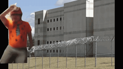 Man In Orange Shirt In Front Of Barbed Wire GIF