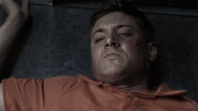 Man In Orange Shirt Laying On Floor Making Funny Face GIF