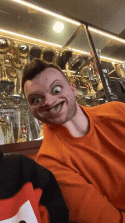 Man In Orange Shirt Making Funny Face With Trophies GIF