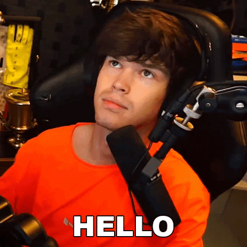Man In Orange Shirt Sitting In Front Of Microphone With Hello Above Head GIF
