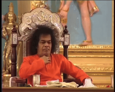Man In Orange Shirt Sitting With Shree Statue GIF