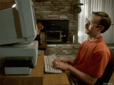 Man In Orange Shirt Typing At Computer GIF