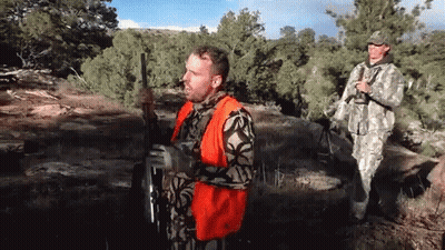 Man In Orange Vest Holding Gun In Field GIF