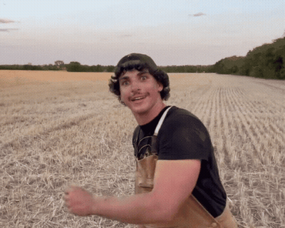 Man In Overalls And Black Shirt Smiling In Field GIF