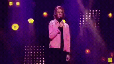 Man In Pink Jacket Holding Microphone On Stage GIF