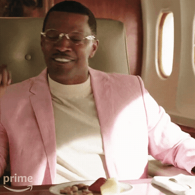 Man In Pink Jacket Sitting At Table With Food And Word Prime GIF