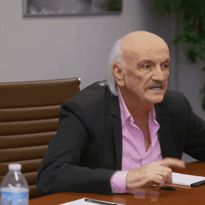Man In Pink Shirt And Black Jacket Sitting At Table GIF