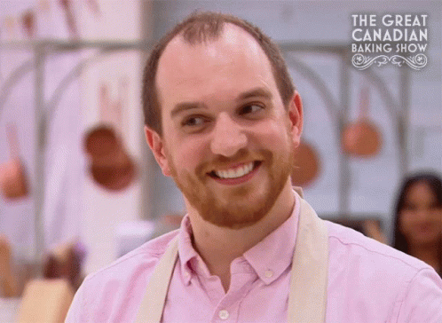 Man In Pink Shirt Smiling In Front Of Baking Show Sign GIF