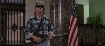 Man In Plaid Shirt Holding Two Guns In Front Of American Flag GIF
