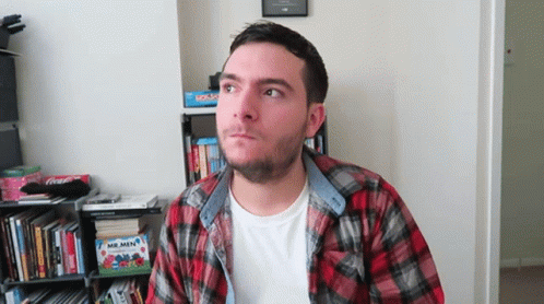 Man In Plaid Shirt In Front Of Bookshelf GIF