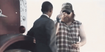 Man In Plaid Shirt Next To Man In Suit And Hat GIF