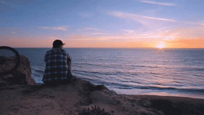 Man In Plaid Shirt On Cliff Overlooking Ocean GIF