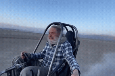 Man In Plaid Shirt Riding Buggy On Dirt Road GIF