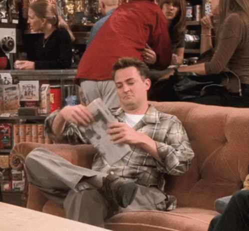 Man In Plaid Shirt Sitting On Couch Reading Paper GIF