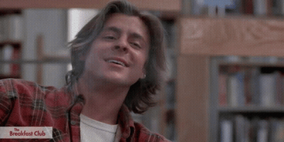 Man In Plaid Shirt Smiling In Front Of Breakfast Club Logo GIF