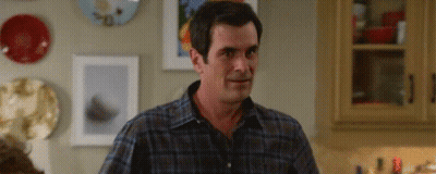 Man In Plaid Shirt Standing In Kitchen Looking At Something GIF