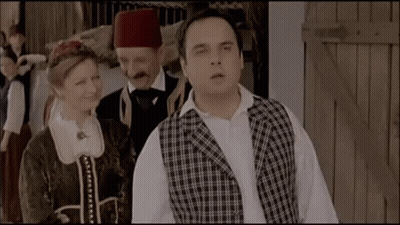 Man In Plaid Vest Beside Woman And Man In Turban GIF