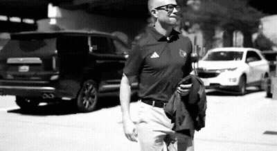 Man In Polo Shirt Walking While Holding Jacket And Looking At Phone GIF