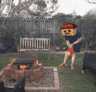 Man In Pumpkin Hat Throwing Chips Into Fire Pit GIF